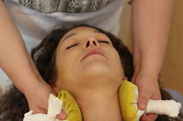 Kräuterstempel-Massage am Nacken einer entspannt liegenden Patientin